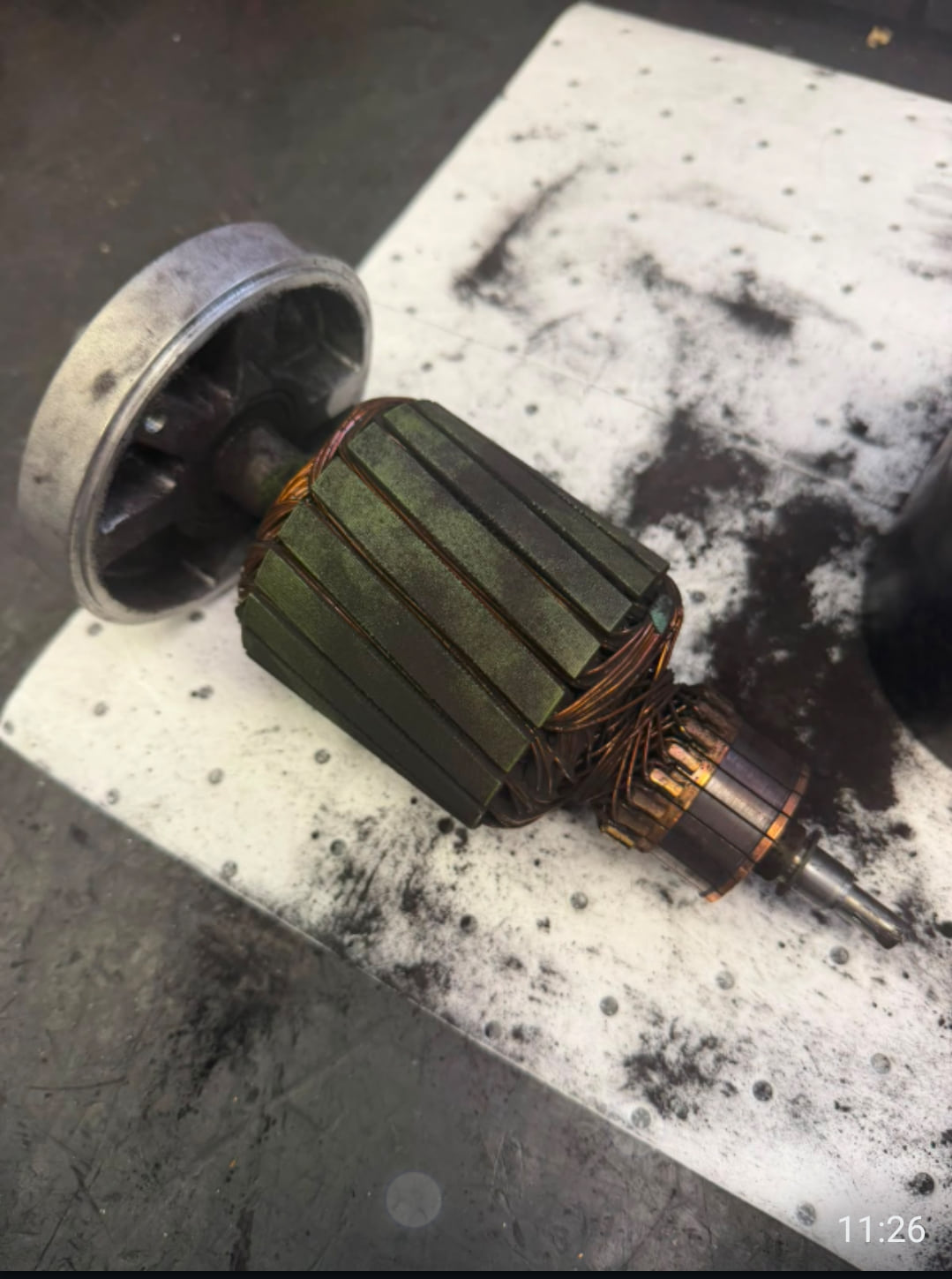 An AutoStore robot drive motor armature withdrawn from its housing on a workshop bench, the commutator blackened and the windings coated in carbon dust