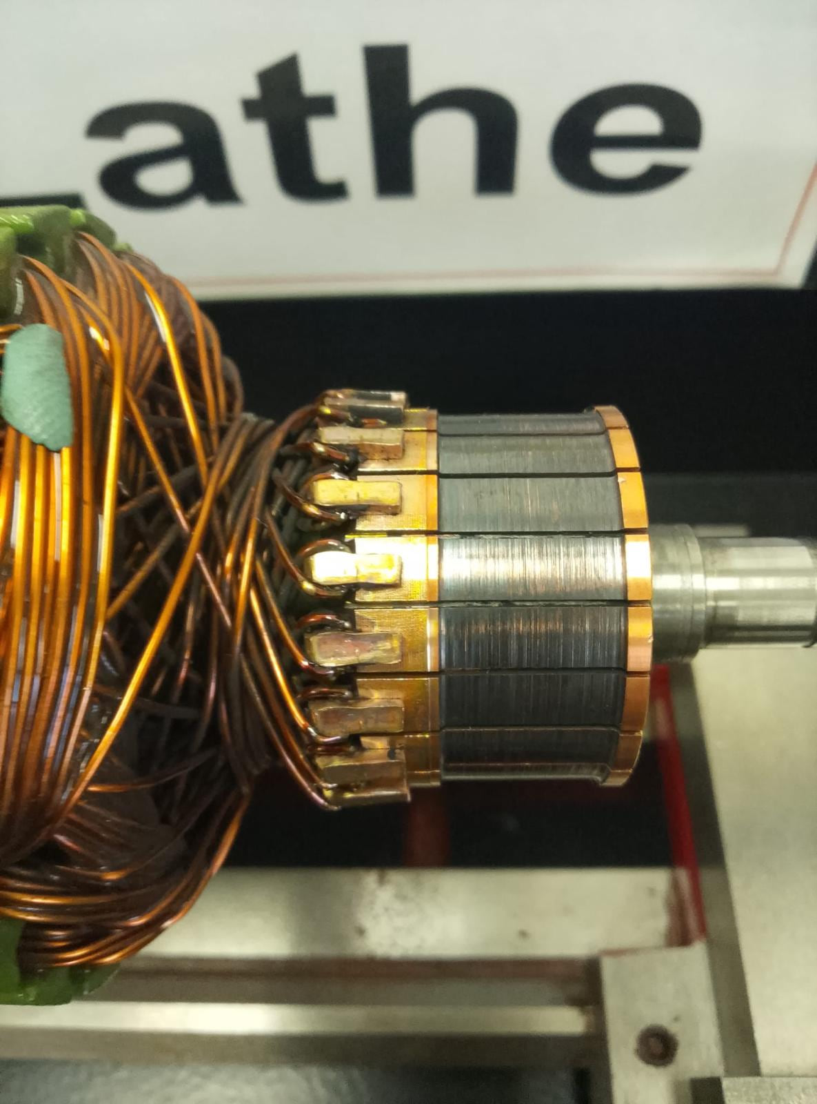 An AutoStore robot drive motor armature mounted between centres in a lathe, its commutator part-machined back to bright copper