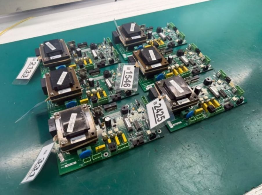 Industrial control boards on a workbench, each tagged with its work order reference