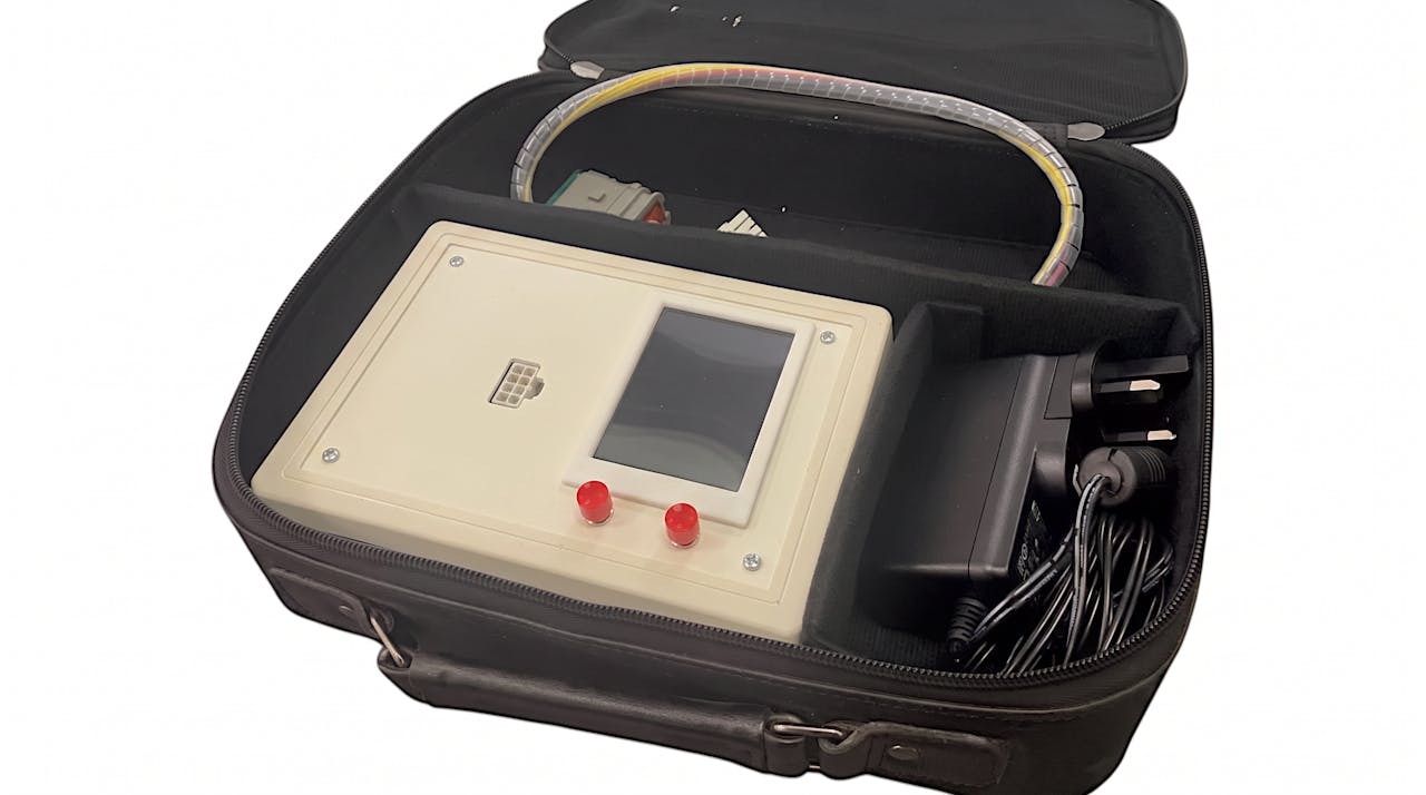 The purpose-built divert switch test rig in its transit case: a bench instrument with a display, two indicator lamps and a loom connector, packed alongside its power supply