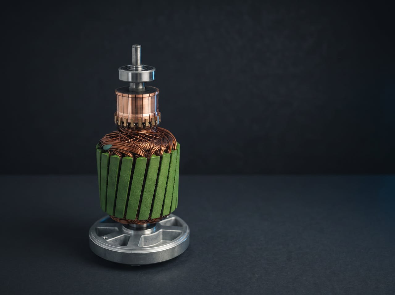 A stripped AutoStore robot drive motor armature on a stand, showing the machined commutator and green slot wedges