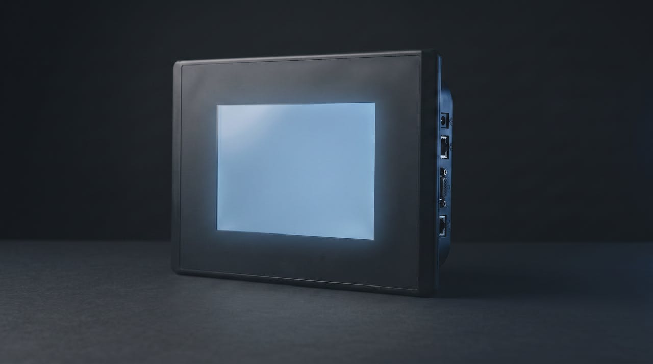 An industrial operator panel with its screen backlit, communication ports along the side
